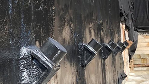 Waterproof coating applied on a concrete wall around metal pipes.