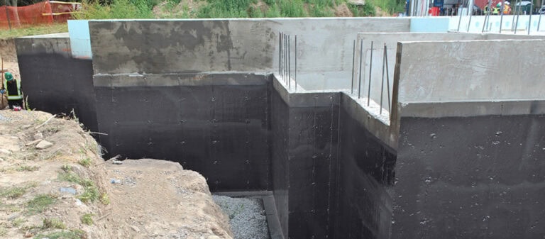 Waterproofing applied to concrete foundation walls at a construction site.