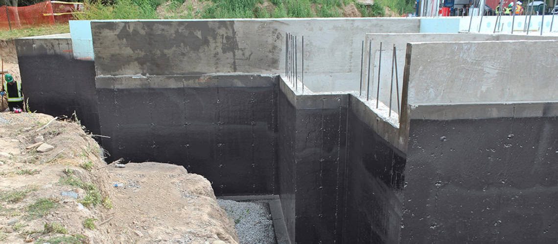 Waterproofing applied to concrete foundation walls at a construction site.